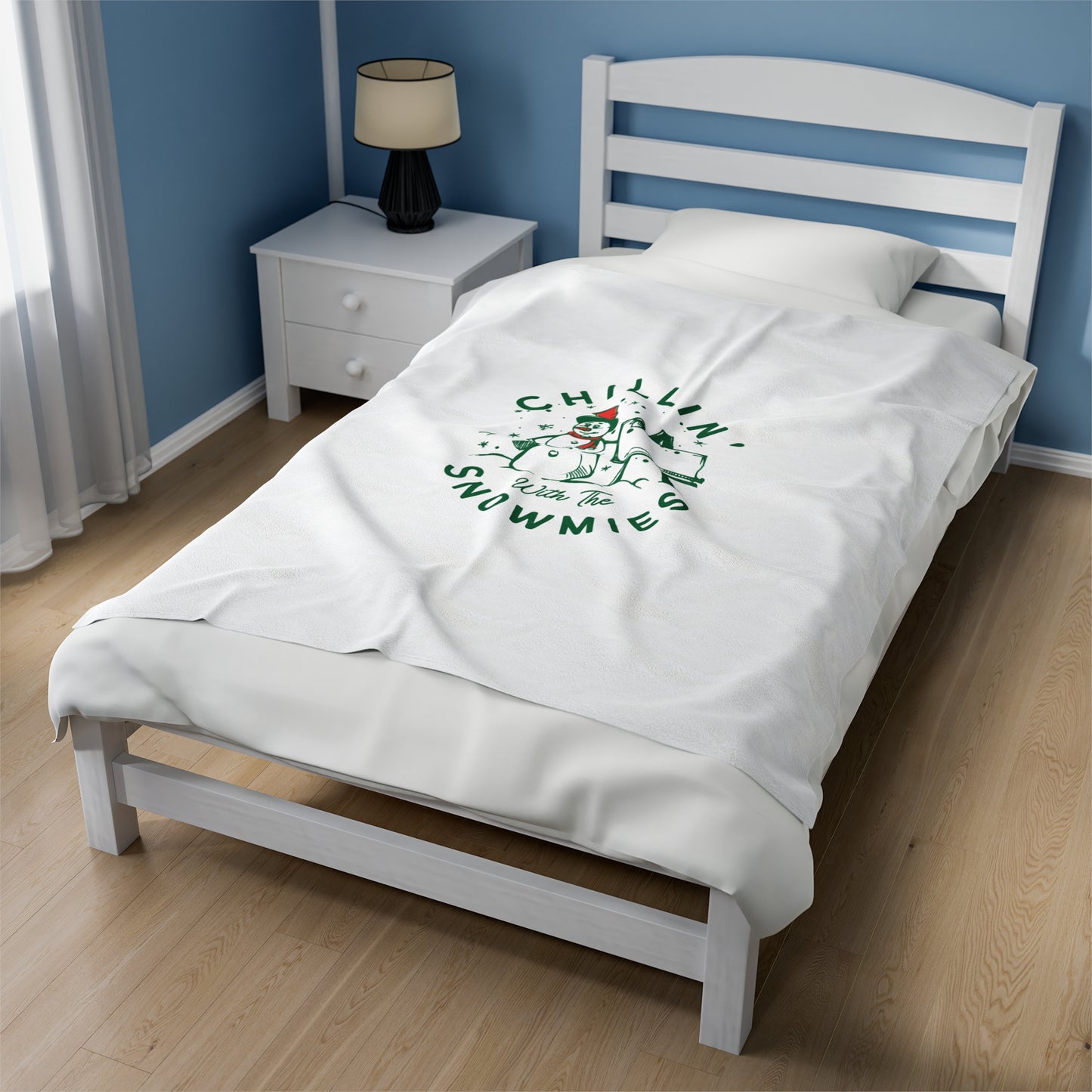 White Christmas blanket with ‘Chillin with the Snowmies’ text draped over a cozy sofa surrounded by festive pillows, lights, and seasonal decor