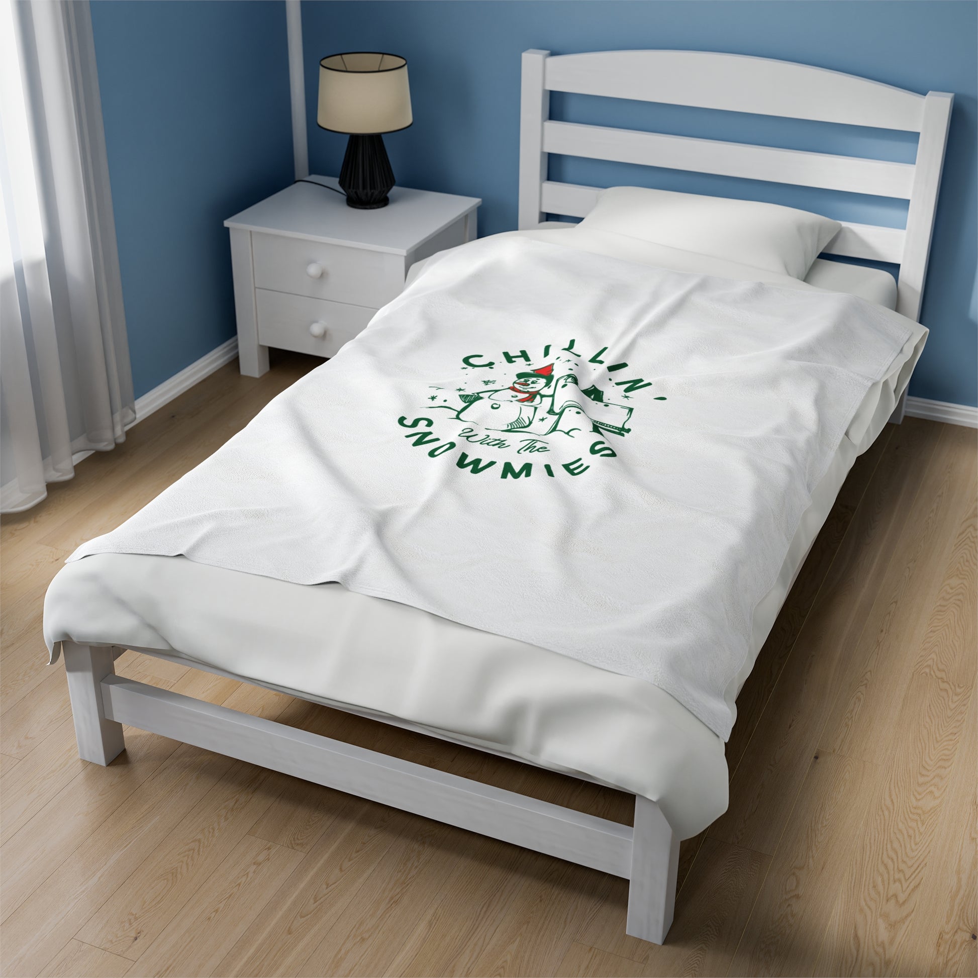 White Christmas blanket with ‘Chillin with the Snowmies’ text draped over a cozy sofa surrounded by festive pillows, lights, and seasonal decor