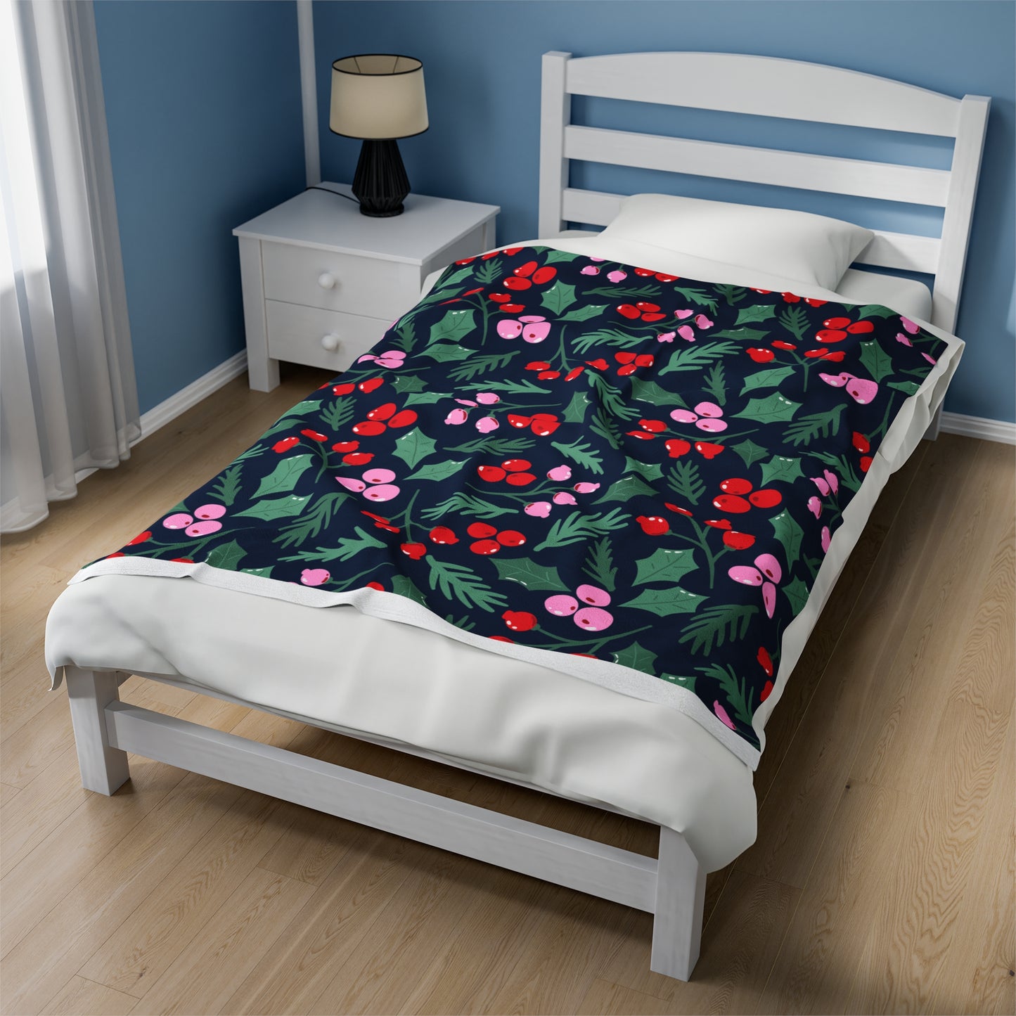 Holiday blanket with pink, red, and green Christmas greenery print draped over festive sofa with cozy pillows and twinkle lights