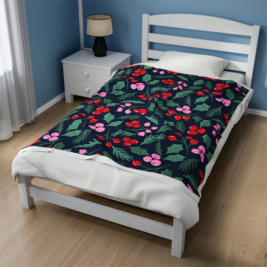 Holiday blanket with pink, red, and green Christmas greenery print draped over festive sofa with cozy pillows and twinkle lights