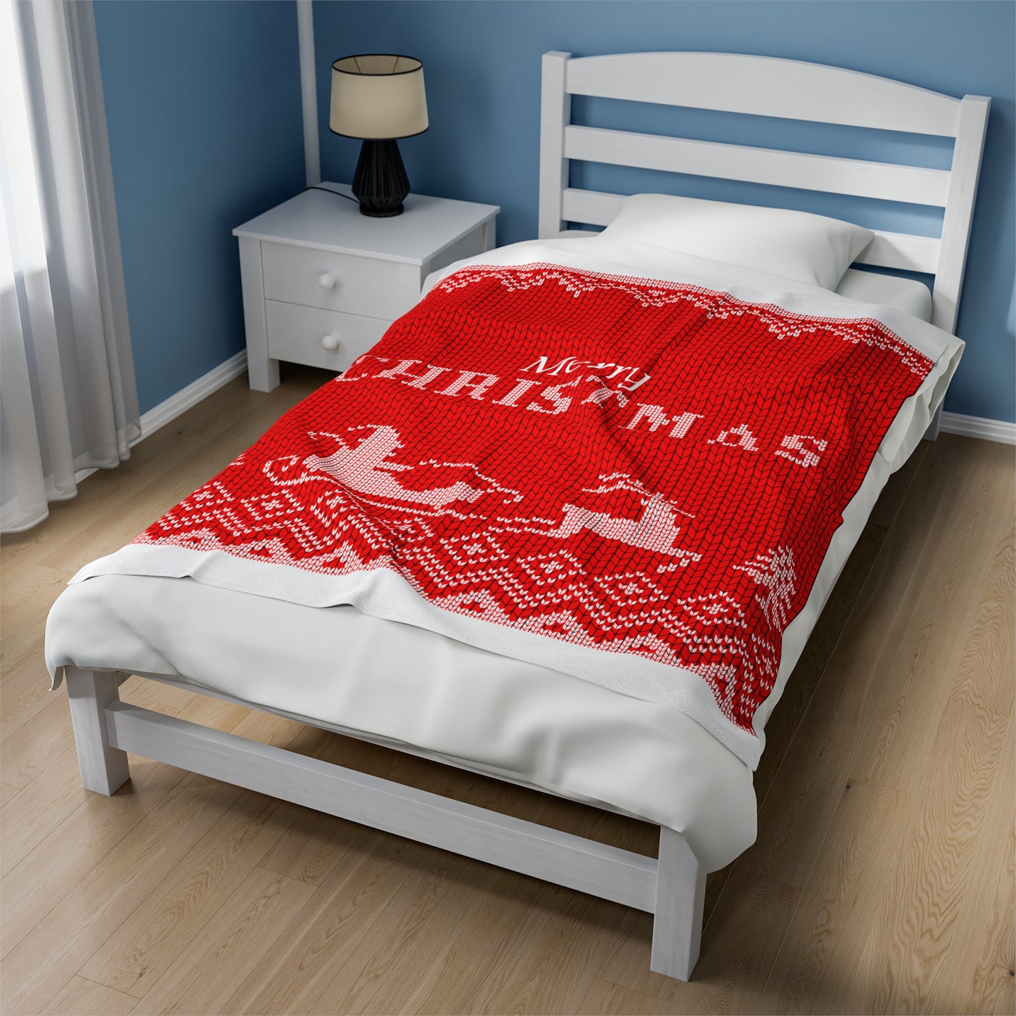 Red holiday blanket with white 'Merry Christmas' script draped over festive sofa with holiday pillows, garland, and twinkle lights
