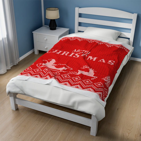 Red holiday blanket with white 'Merry Christmas' script draped over festive sofa with holiday pillows, garland, and twinkle lights
