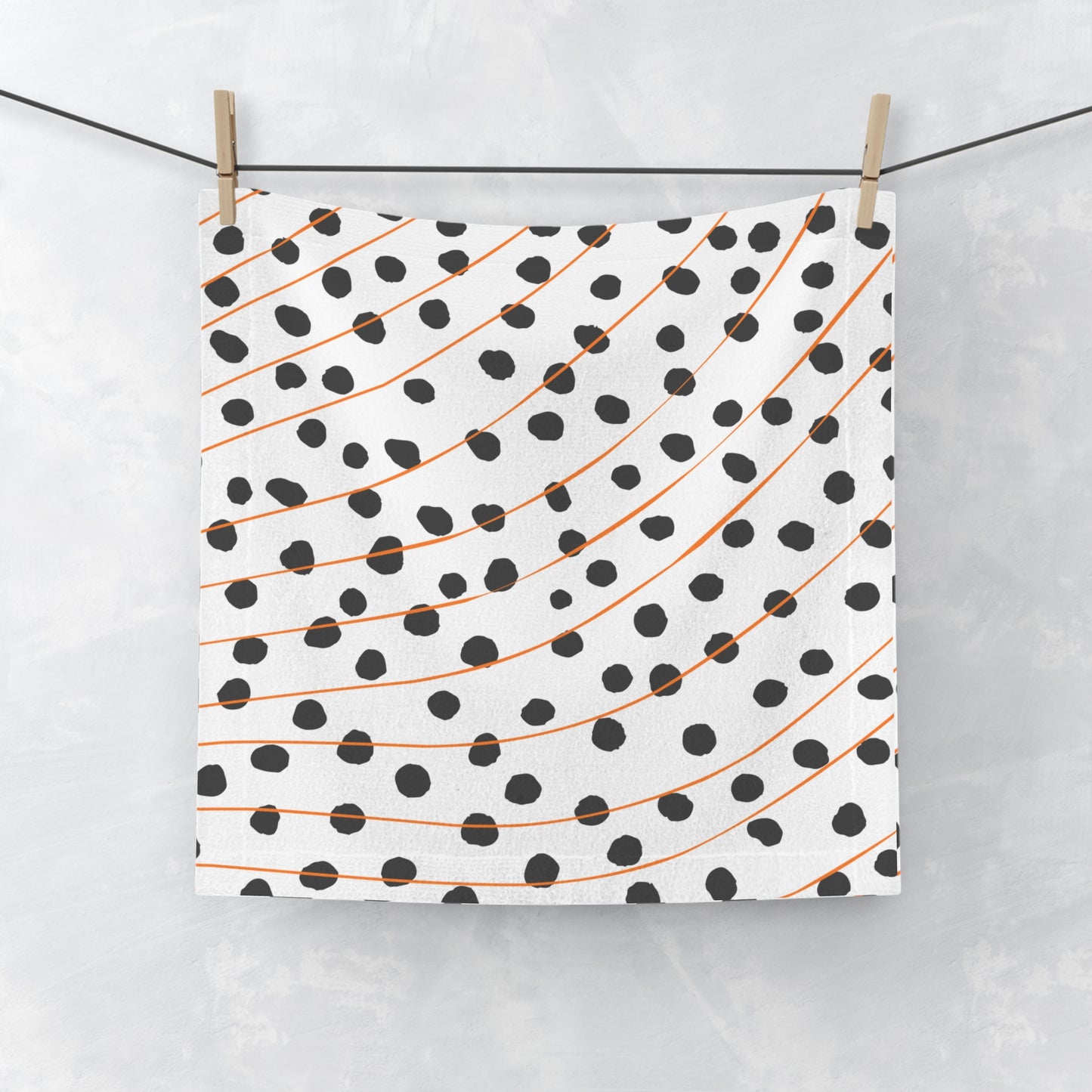 Orange and black polka dot face towel with modern abstract pattern, laid flat on white surface