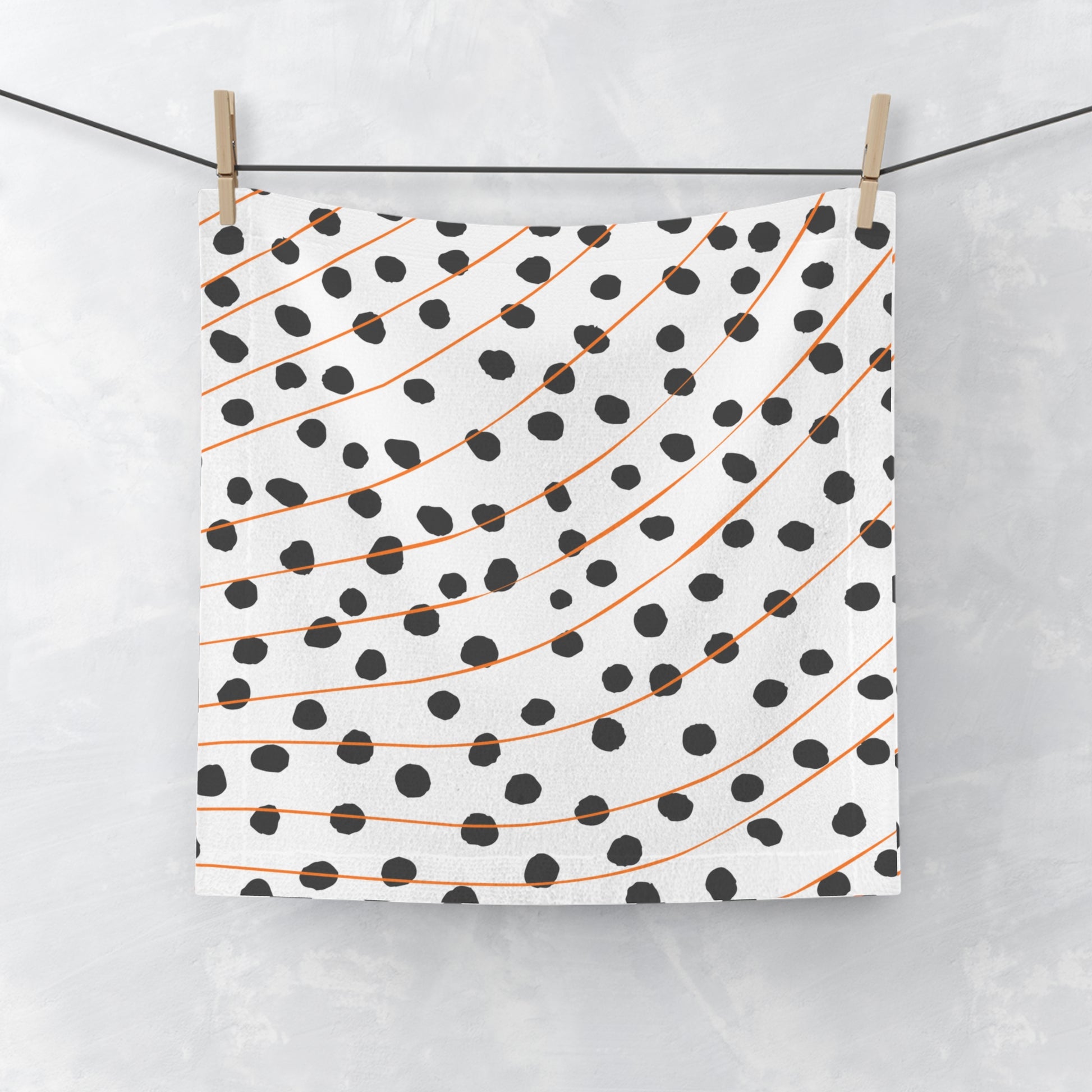 Orange and black polka dot face towel with modern abstract pattern, laid flat on white surface