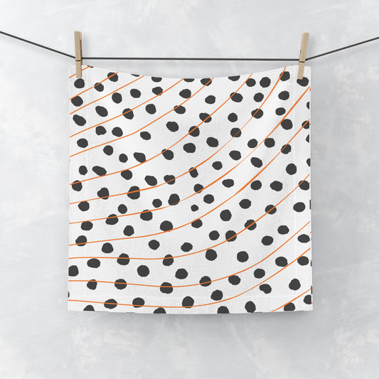 Orange and black polka dot face towel with modern abstract pattern, laid flat on white surface