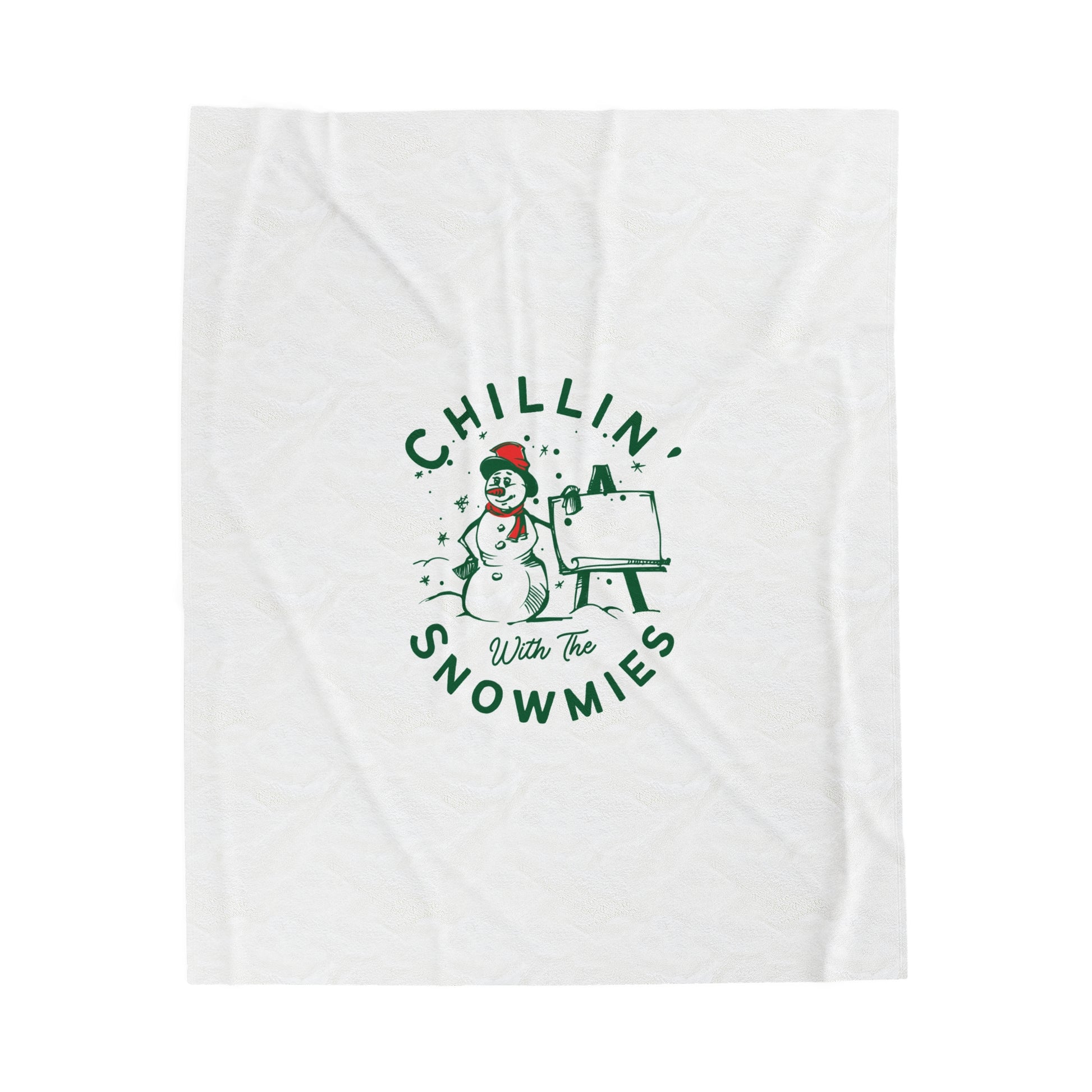 Flat lay of white holiday blanket featuring bold ‘Chillin with the Snowmies’ lettering, folded neatly on soft festive surface