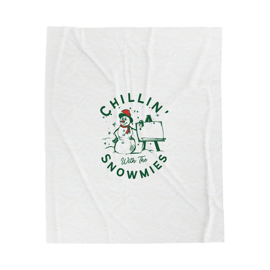 Flat lay of white holiday blanket featuring bold ‘Chillin with the Snowmies’ lettering, folded neatly on soft festive surface