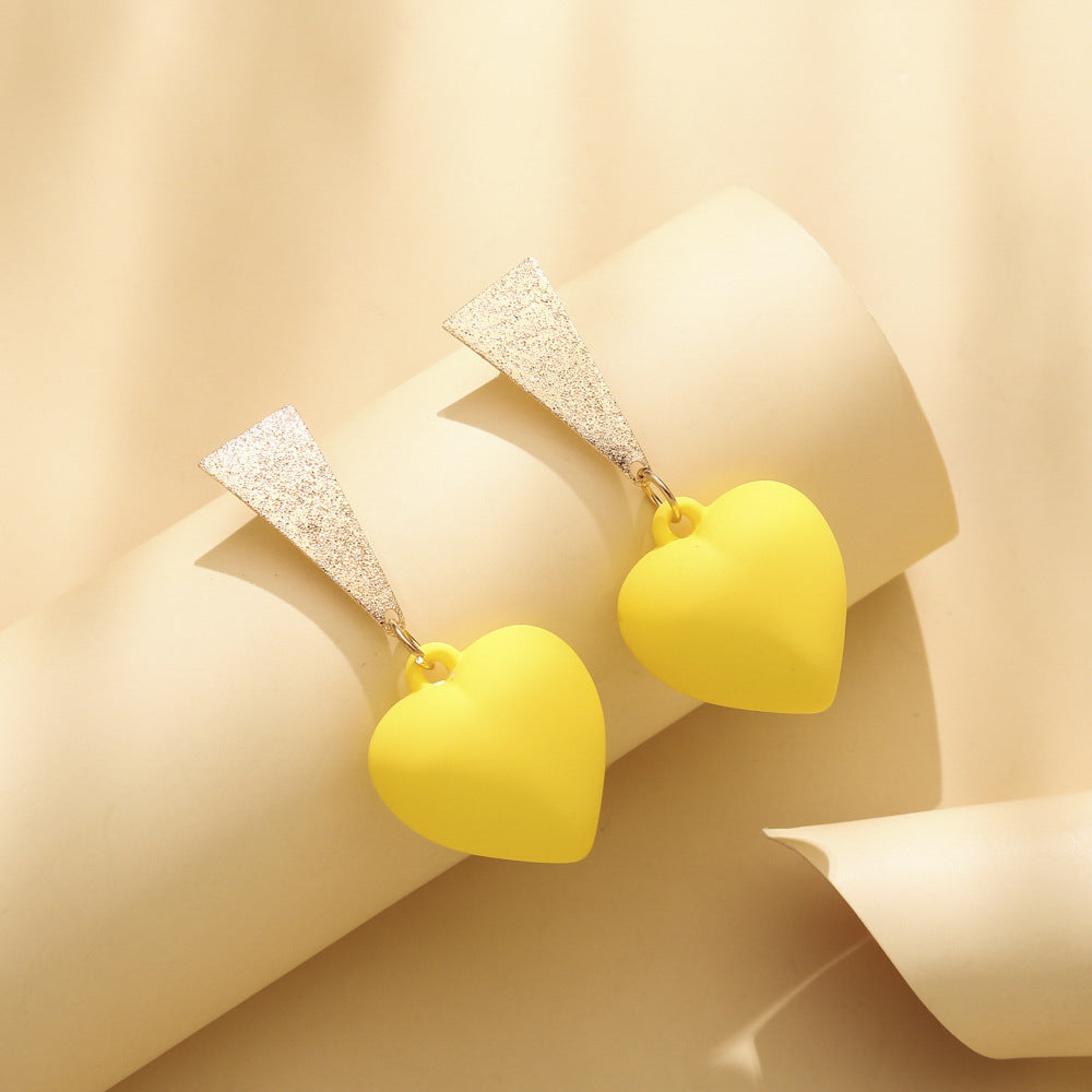 Pair of yellow heart-shaped earrings on soft textured background